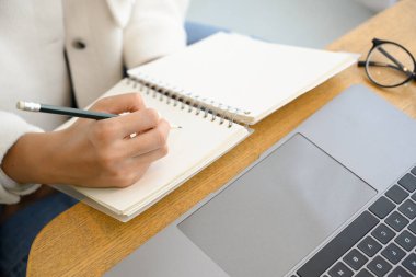 Kırpılmış resim, kız üniversite öğrencilerinin çevrimiçi öğrenme çalışmaları dizüstü bilgisayardan ve boş spiral not defteri üzerine dersler alıyor..