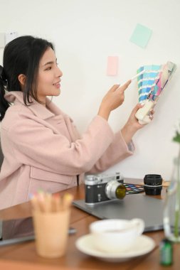 Çekici Asyalı kadın fotoğrafçı ya da grafik tasarımcısı masasında renk örnekleri tutuyor.