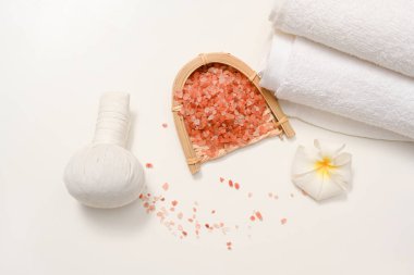 Himalaya tuzlu spa kompozisyonları, masaj topu, havlular ve beyaz arka planda frangipani çiçeği.