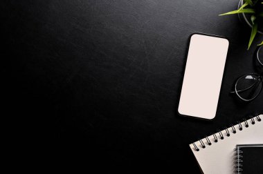 Siyah çalışma alanı arka planı fotokopi alanı, akıllı telefon beyaz ekran modeli, spiral not defteri ve aksesuarları. Üst görünüm, düz uzanma