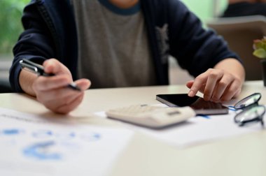 Kesilmiş resim, akıllı telefon kullanan ve muhasebe ödevi üzerinde çalışan kız üniversite öğrencisi..