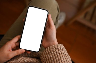 Üst manzara, modern bir cep telefonu dokunmatik ekranının kadınların elindeki bir maketi. Kadın oturma odasında rahatlıyor ve akıllı telefon kullanıyor..