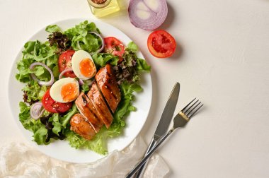 Sağlıklı yeşil organik salata sebzeleri ve beyaz masa arkasında ızgara bbq tavuk göğsü..