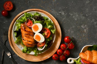 Üst manzara, düz yatak, sağlıklı ketojenik yemek menüsü, haşlanmış yumurtalı ızgara tavuk göğsü ve şık gri arka planda taze salata sebzeleri..