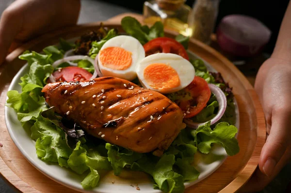 Yakın plan, kadın aşçı bir tabak lezzetli ızgara Teriyaki tavuk göğsü salatası ve haşlanmış yumurta servis ediyor.