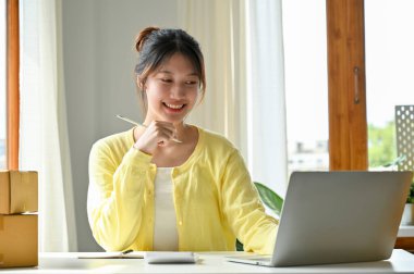 Asyalı çekici bir bayan dizüstü bilgisayar kullanıyor, kendi online pazarlama stratejisini tasarlıyor ve düşünüyor..