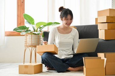 Startup business, Female online seller compares the delivery code number on the website and the box in her living room.