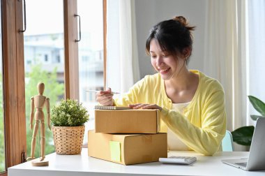 Çekici Asyalı internet sahibi kadın paketini hazırlıyor ve ürünü evde bir paket kutusuna koyuyor..
