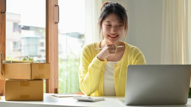 Akıllı ve başarılı Asyalı genç satıcı dizüstü bilgisayar kullanıyor, işi için online stratejisini planlıyor. E-ticaret iş konsepti