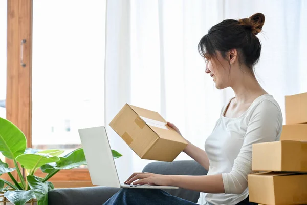 Female business startup entrepreneur typing the shipping code on her online store page, updating shipping status via laptop computer.