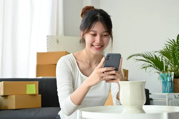 Attractive Asian millennial woman enjoy shopping on online shopping application platform on her smartphone at home.