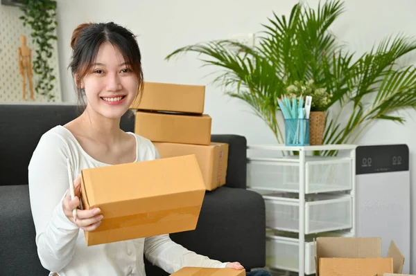Smile Asian millennial female online shop owner packing her stuff in the living room, checking the parcel boxes. SME small business entrepreneur