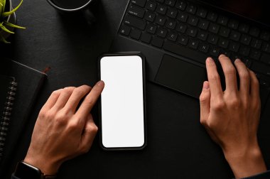 Top view, flat lay, A man using smartphone and typing on wireless tablet keyboard in black table background. Phone white screen mockup.