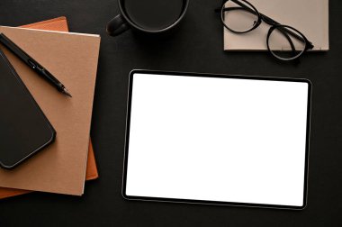 Modern stylish black workspace background with tablet touchpad white screen mockup, stationery, a cup of coffee, glasses and stuff. top view