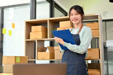 Güzel ve başarılı Asyalı bayan girişimci şirket sahibi elinde bir dosya kağıdıyla depoda duruyor. Küçük işletme girişimcisi.