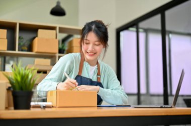 Mutlu Asyalı kadın girişimciler paket kutuları üzerinde çalışır, makbuzlar ve müşteri adresleri yazar. KOBİ iş sahibi kavramı