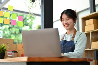 Mutlu Asyalı genç bayan moda dükkânı sahibi müşterisinden gelen mesajları cevaplamak için dizüstü bilgisayarını kullanıyor, müşteriden iyi bir eleştiri alıyor. Küçük işletme kavramı