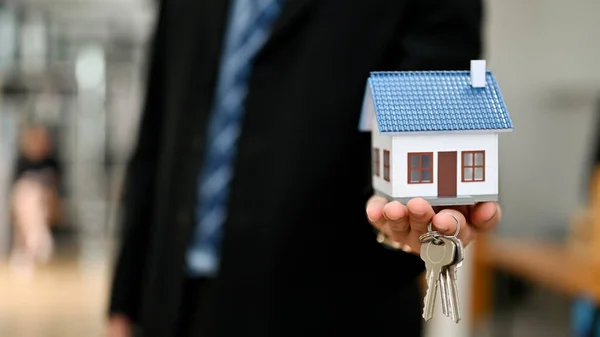 A house model mockup on a businessman\'s hand with blurred background. House insurance, property investment concept
