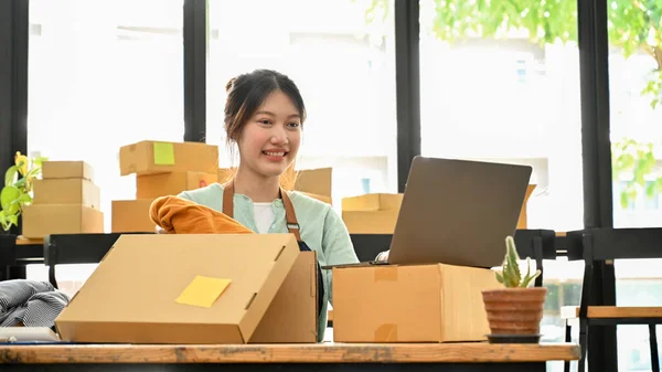 Female clothes shop owner packing clothes in a brown parcel box, preparing customer\'s order to ship. SME fashion business.