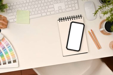 Modern minimal white workspace with smartphone blank screen mockup on notepad, keyboard computer, stationery and copy space on white table background. top view