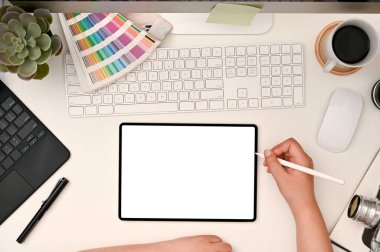Modern graphic designer workspace top view, flat lay, with a female using stylus pen drawing on digital tablet screen. Tablet white screen mockup.