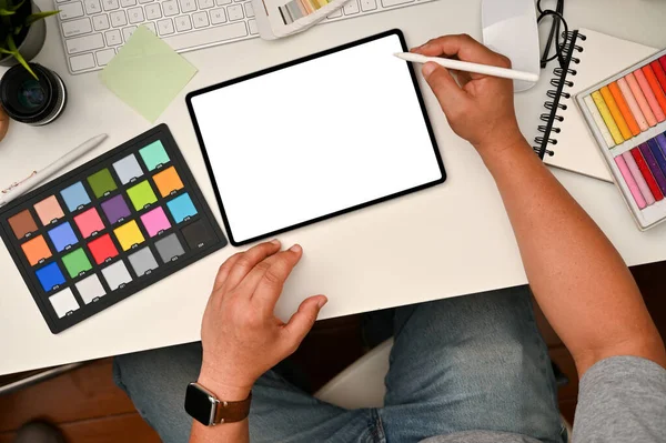 Graphic designer workspace concept, Male graphic designer or photo editor using digital tablet at his office desk. colour checker, stationery and stuff on white table, top view.