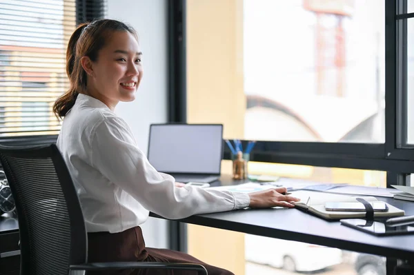 Happy Asian millennial businesswoman smiling and working at her modern office desk. Businesspeople portrait