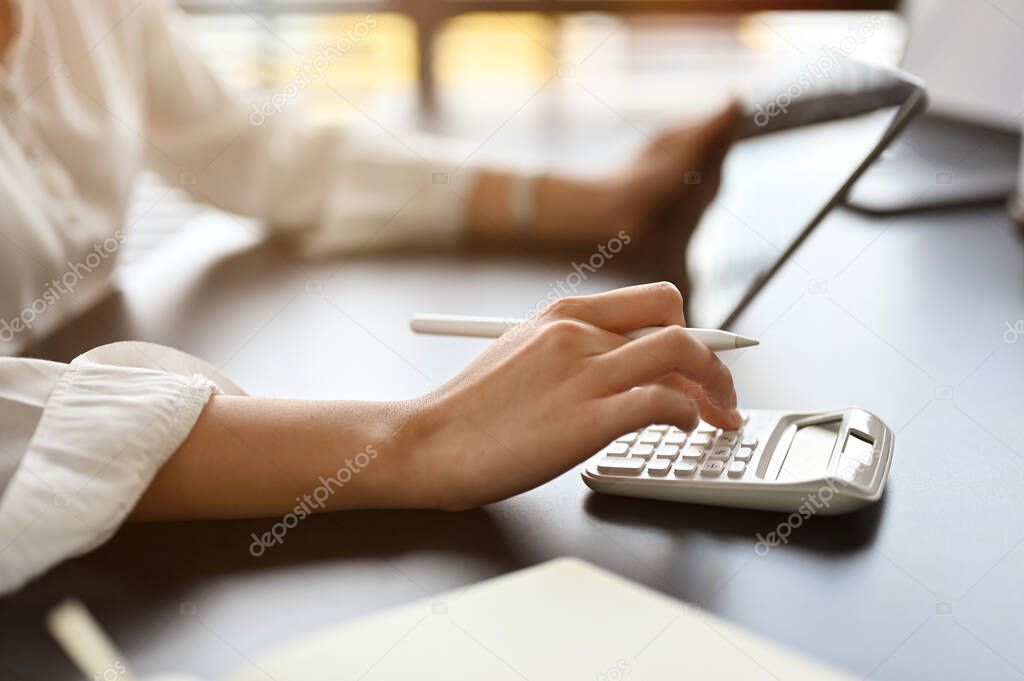 Businesswoman or female accountant using calculator at her office desk. focus hand, cropped image