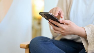 Kadın oturma odasında mola veriyor, internet içeriğini izliyor, akıllı telefon kullanıyor. Kırpılmış, yakın plan