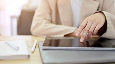 A businesswoman in minimal casual suit sitting at her office desk and using digital portable tablet computer. cropped, close-up image
