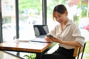 Güzel Asyalı kadın iş kadını ofisteki parlak çalışma alanında akıllı telefon kullanıyor..