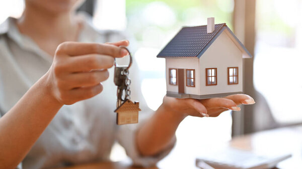 Cropped image, Female real estate agent at the office desk with house model and house keys in her hands.