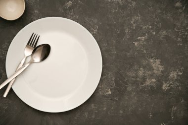 Boş beyaz ve temiz tabağı, çatal bıçak ve kaşığı gri arka planda kopyalama alanı olan minimal basit restoran yemek masası. en üstteki görünüm