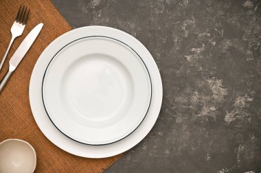 Kahverengi servis altlığı, gümüş çatal bıçak takımı ve şık koyu gri arka planda en az beyaz tabak. en üstteki görünüm