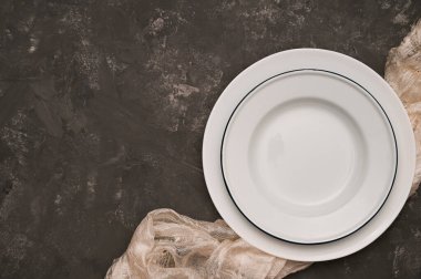 Beyaz masa örtüsü üzerine boş beyaz tabak ve koyu gri arkaplan üzerine kopyalama alanı ile modern minimal yemek masası ayarlama arka planı. en üstteki görünüm