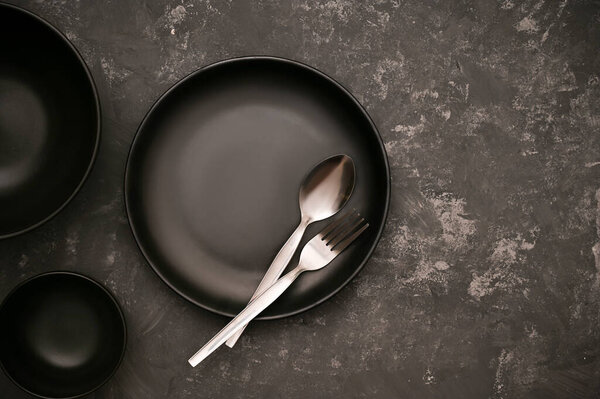 Stylish black empty plate mockup with silverware and sauce bowl on modern stylish dark grey background. top view
