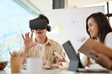 Milenyum Asyalı erkek bir VR oyunu oynuyor, VR kulaklık takıyor, ofiste yeni bir yenilik deniyor..