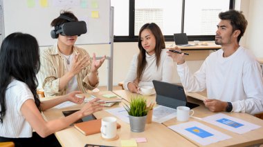 Bir grup teknoloji geliştirici ofiste toplanıp sanal oyunun yeni versiyonunu VR gözlükleri üzerinde tartışıp test ediyorlar..