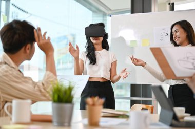 Toplantıda projesini sunan Asyalı bir kadın grafik geliştirici, VR oyununu test eden bir kadın kullanıcı. Sanal gerçeklik yeniliği. 