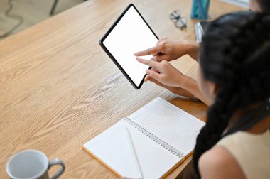 Yakın plan görüntü, dijital tablet dokunmatik ped kullanan sevimli küçük Asyalı kız ev ödevi için internetten bilgi arıyor, annesiyle aynı masada oturuyor..