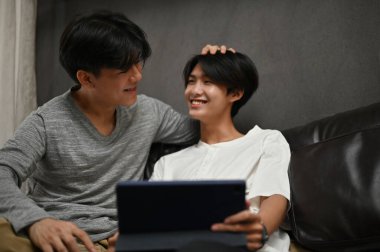 İki Asyalı genç eşcinsel erkek oturma odasında rahatlar, dijital tablette film izlemenin tadını çıkarırlar. LGBT aşığı sevgisi.