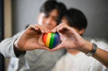 Yakından bakınca, iki Asyalı eşcinsel çift ellerinde gökkuşağı kalbiyle elleriyle kalp şekli oluşturuyorlar. LGBT aşk simgesi.
