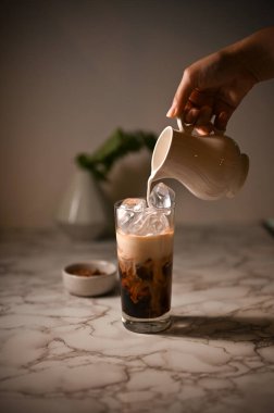 Yakın plan görüntü, bayan baristanın eli buzlu kahveye taze süt dökerek buzlu latte yapıyor..