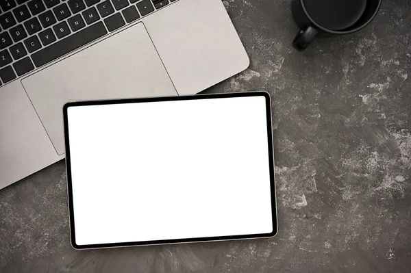 Stylish office desk workspace top view with laptop, coffee cup and tablet white screen mockup on textured grey background.