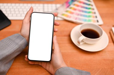 Modern grafik tasarımcısının ofis masasının üzerinde akıllı telefon beyaz ekran modeli tutan kadın eller. Resmi kapat.