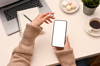 Ofis masasında akıllı telefonunu kullanan güzel bir kadın. Cep telefonu beyaz ekran modeli. en üstteki görünüm