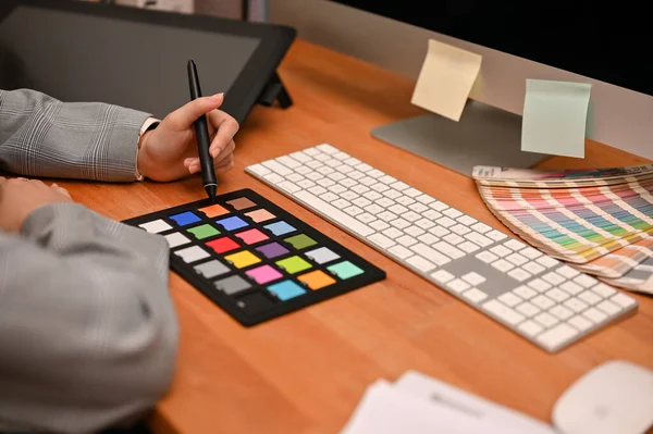 Female freelance graphic designer working at her home office desk. colour checker board, keyboard, graphic tablet and colour swatches chart on table. cropped image