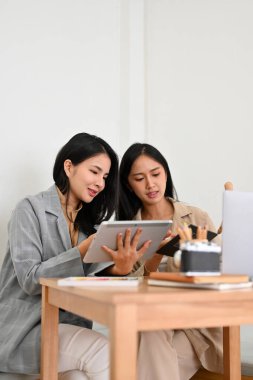 İki güzel Asyalı genç iş kadınının portresi kafede uzaktan kumandalı olarak çalışıyor, taşınabilir tablet kullanıyor ve iş hakkında tartışıyorlar..