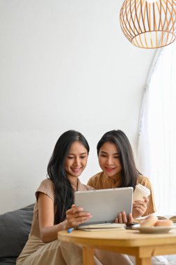 İki güzel Asyalı kadının portresi kafede dinleniyor, konuşmaktan hoşlanıyor ve birlikte tablet ekranda ilginç bir şeyler izliyorlar..