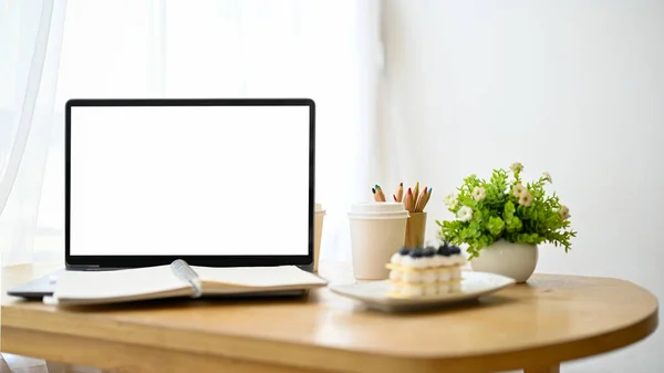 ノートパソコンのホワイトスクリーンモックアップ スパイラルノートブック コーヒー ケーキ 木製テーブルの装飾とワークスペースのクローズアップ — ストック写真